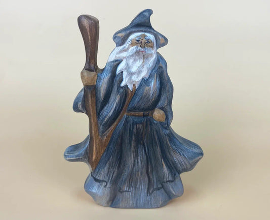 Front view of wooden wizard figurine with grey hat and robes with a long beard and wielding a staff
