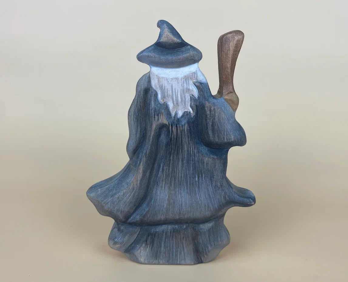 Back view of wooden wizard figurine with grey hat and robes with a long beard and wielding a staff